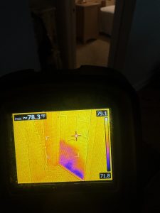 FLIR thermal image of hallway and bathroom showing water saturation in the floor and a faint tub outline.