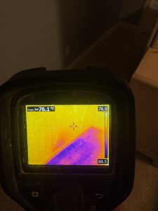 FLIR thermal image showing moisture around an electrical outlet and in the carpet of a hallway during leak detection.